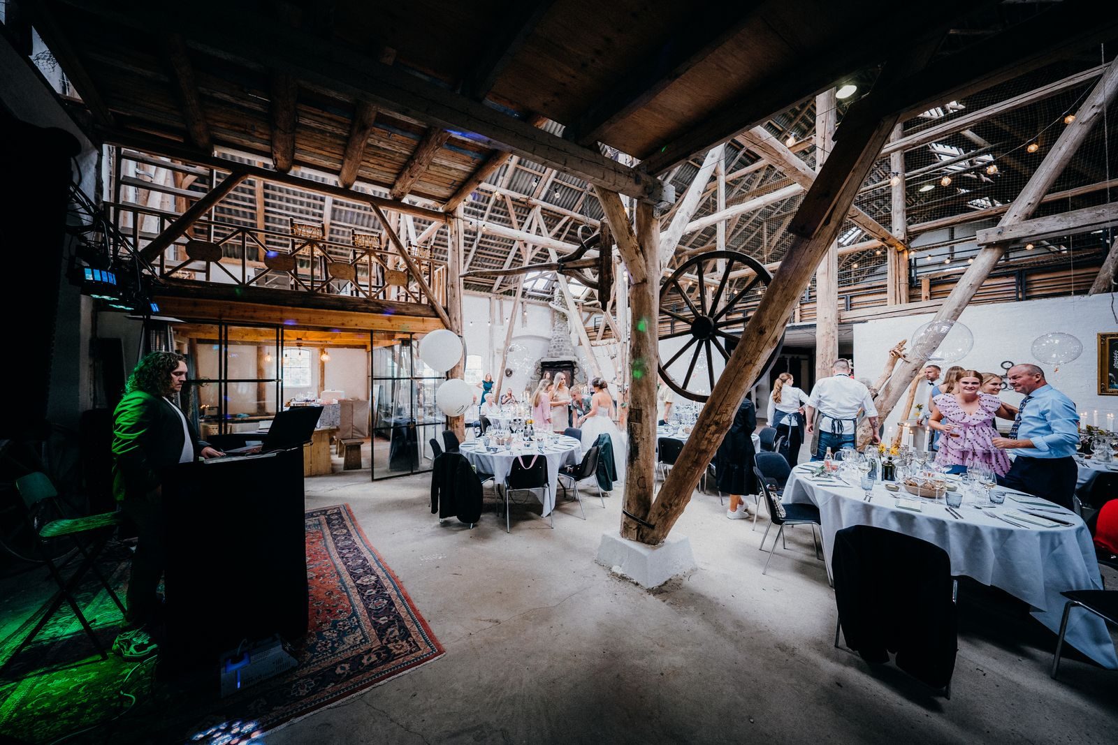 DJ booth set up at a barn wedding reception with guests at banquet tables