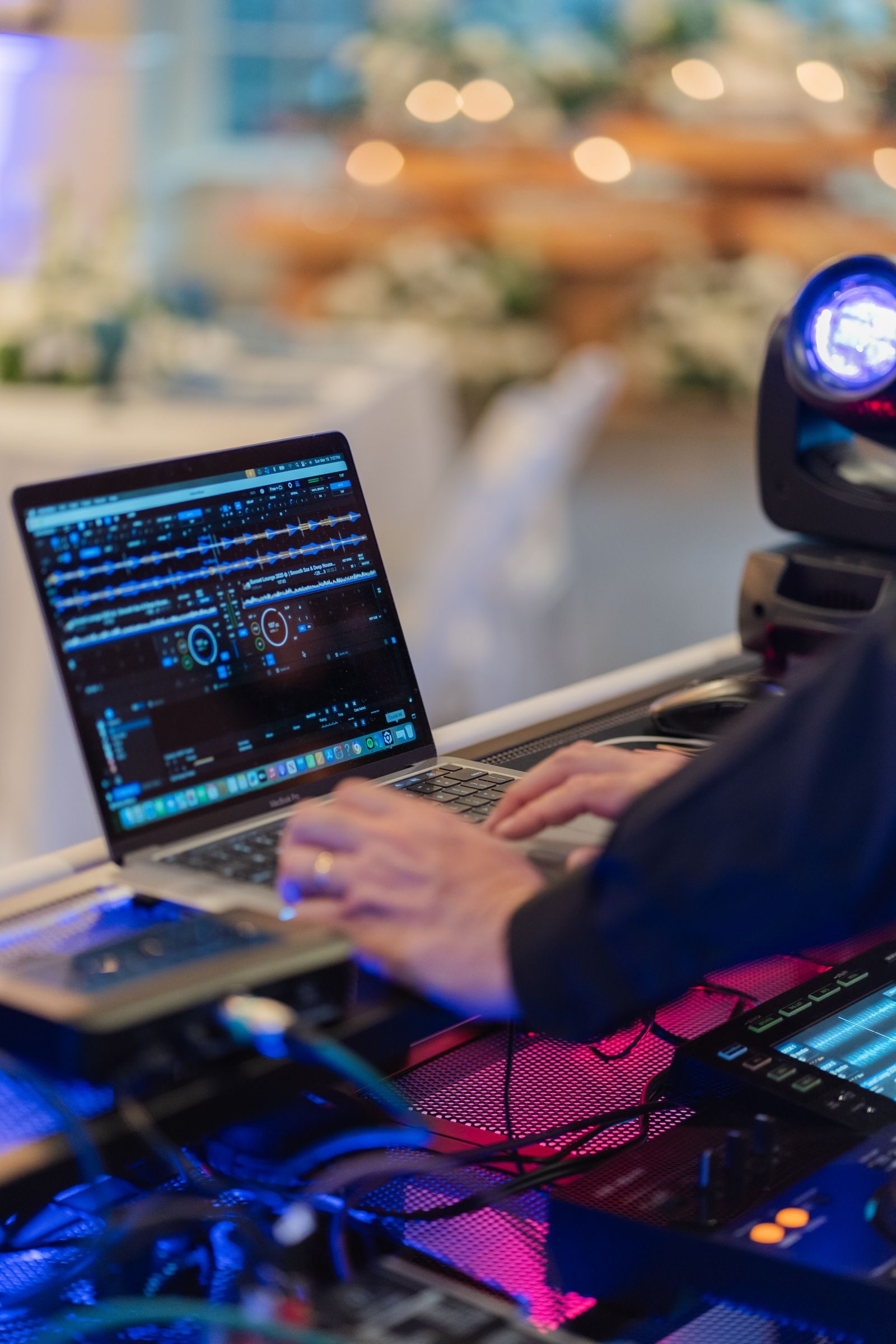 DJ's hands on a laptop and controller with reception tables behind